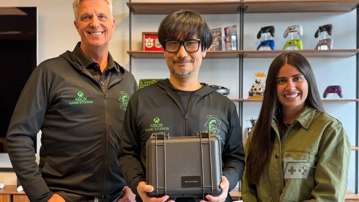 Fotografía de Hideo Kojima en el centro con una caja que dice "Xbox for Kojima" posando junto a Matt Booty y Asha Sharma a los lados.